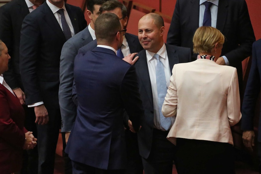 Josh Frydenberg shakes hands with Andrew Bragg, who has his hand on his shoulder.