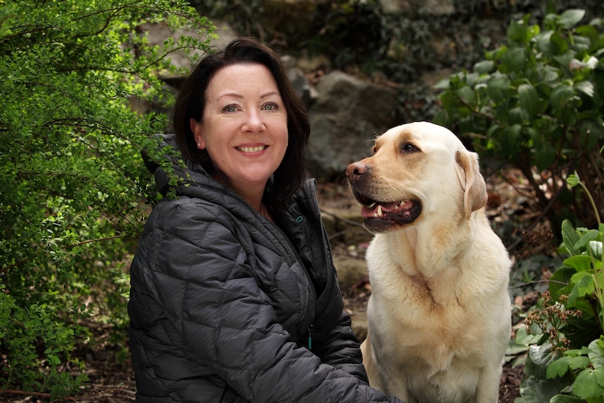 Woman sits next to Labrador dog.