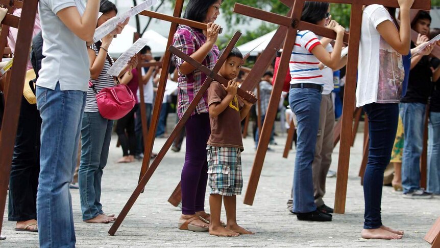 A boy and his family carry crosses to one of the Stations of the Cross in Manila