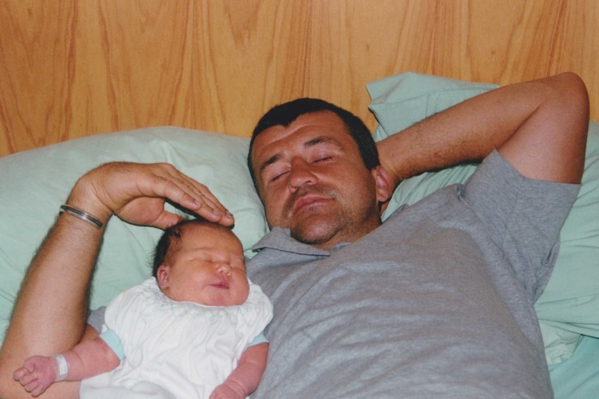 A man lays next to a newborn baby girl on a hospital bed.