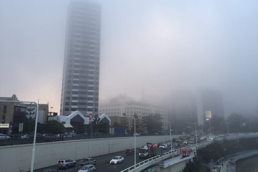 A tall building in Brisbane partially disappears in early morning fog