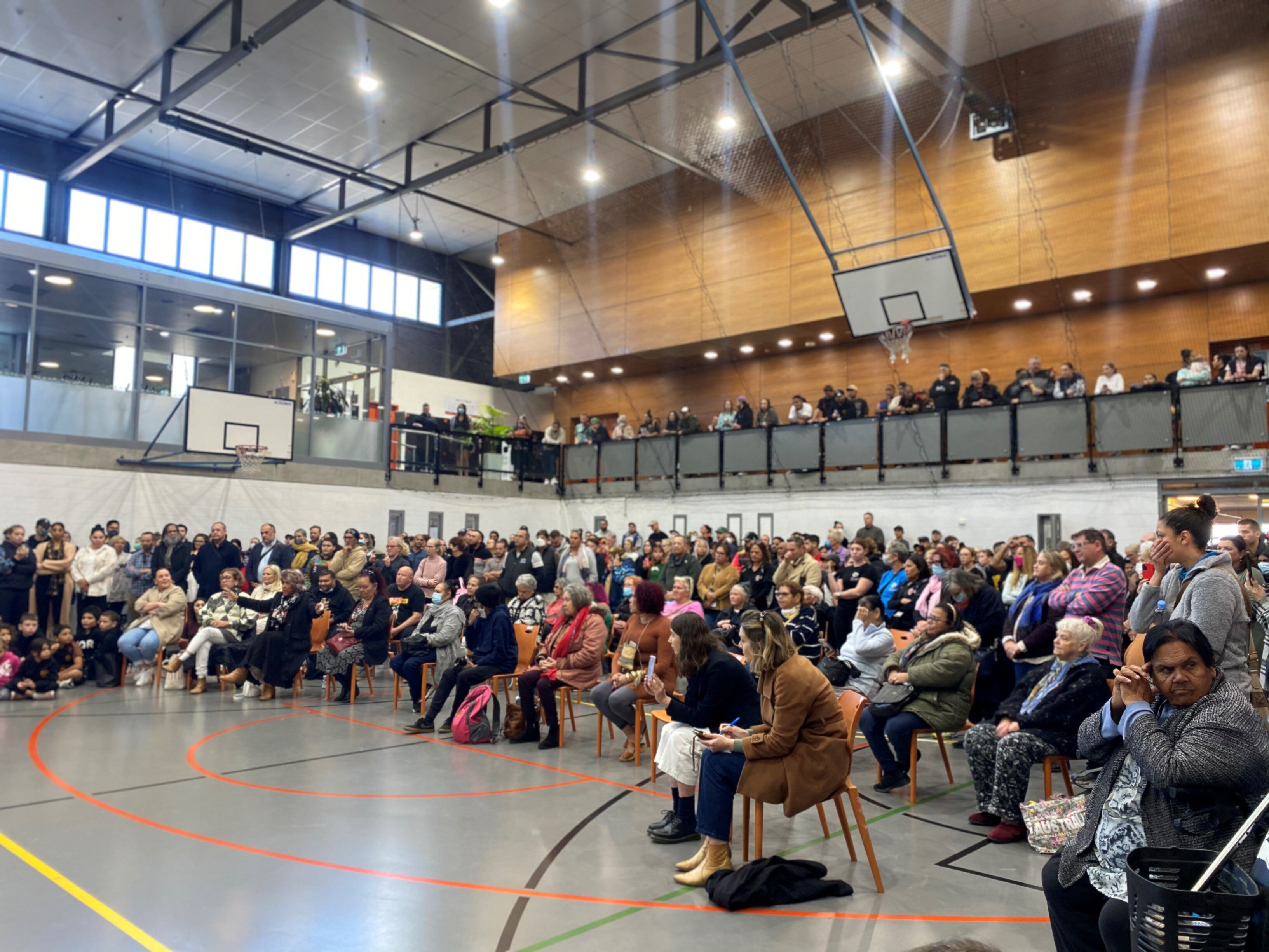 A group of people sit on chairs inside a basketball court
