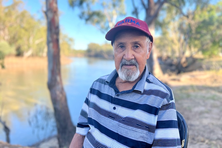 Uncle Colin, wearing a polo shirt and red cap, looks at the camera with the Murray River behind him.