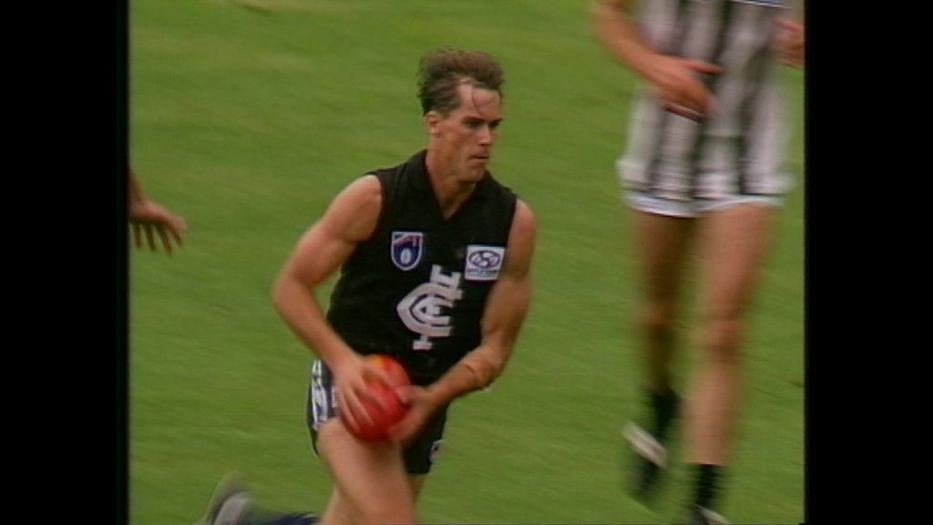 Archival image of a man running with a red ball during a game of AFL.