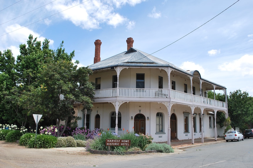 A two story white building with a decorative railing on the balcony of the second floor and a green tin roof