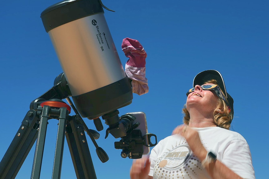 A woman looks up wearing glasses and standing next to a telescope
