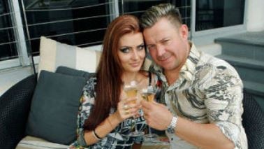 Vitali Roesch and his wife Marnya Kosukhina sitting on a outside couch with champagne in hand.