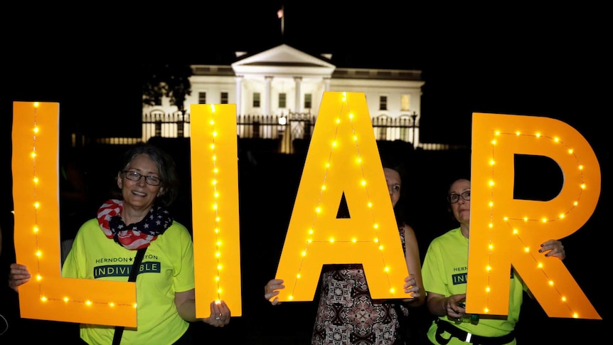 Protesters hold up letters that spell the word liar with the White House illuminated in the background