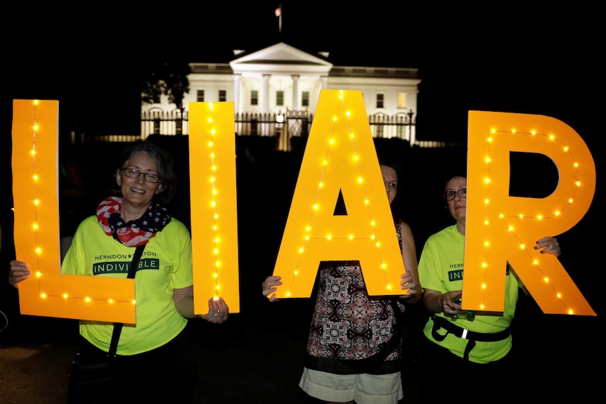 Protesters hold up letters that spell the word liar with the White House illuminated in the background
