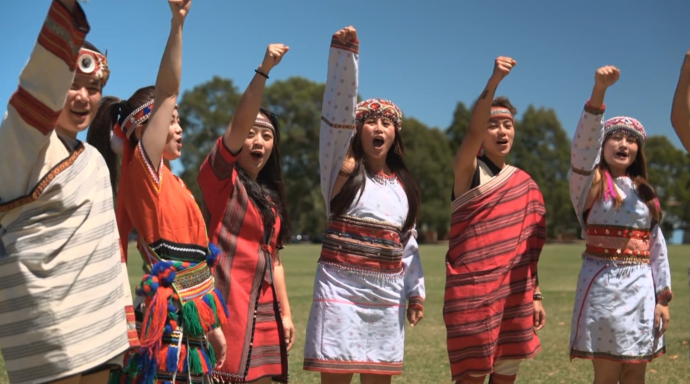 Seis taiwaneses-australianos vestindo trajes tradicionais têm os braços levantados no ar, torcendo