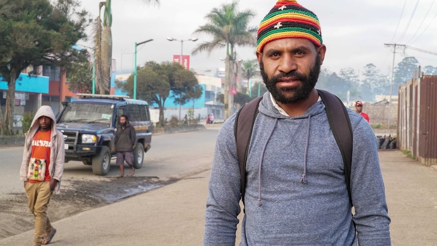 Webster Kerro stands on the streets of Mount Hagen and looks at the camera while a young person walks in the background.