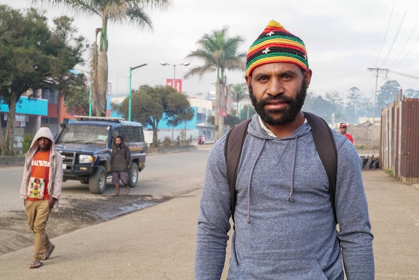 Webster Kerro stands on the streets of Mount Hagen and looks at the camera while a young person walks in the background.