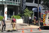 An office block with firefighter crews out front and a Greek flag waving.