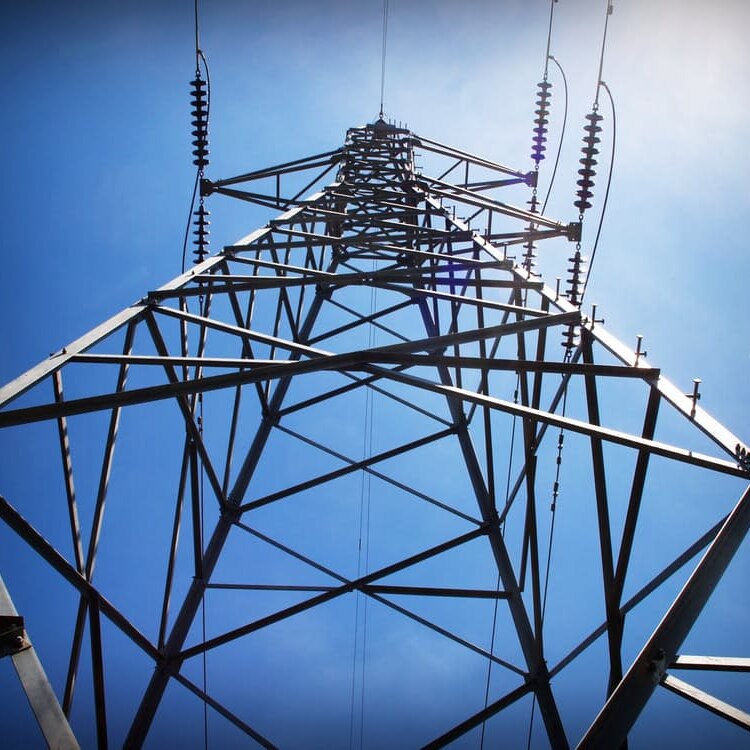 An electricity tower, as seen from below, rises into a blue sky.