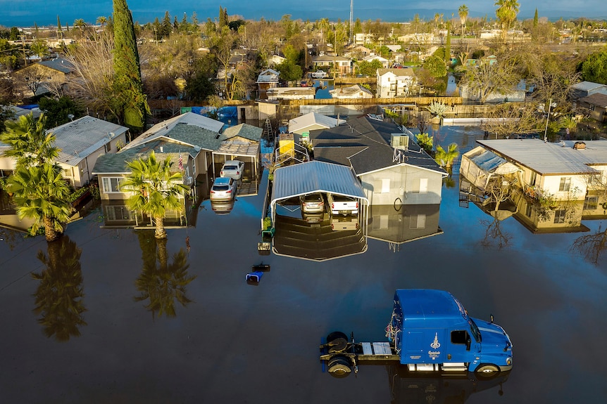 Numerous houses partly under water with a blue truck in the middle of flood water