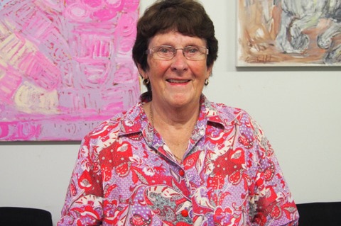 Derby West Kimberley Shire President Elsia Archer stands wearing a pink and red shirt in front of a wall with paintings on it.