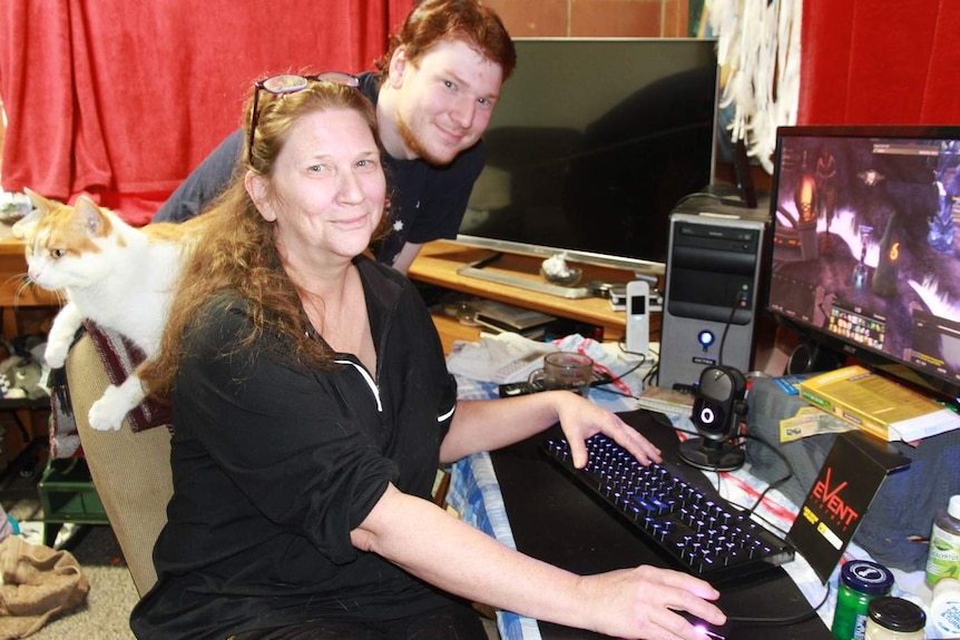 A mother and son - plus a cat - sit in front of a computer and play video games.