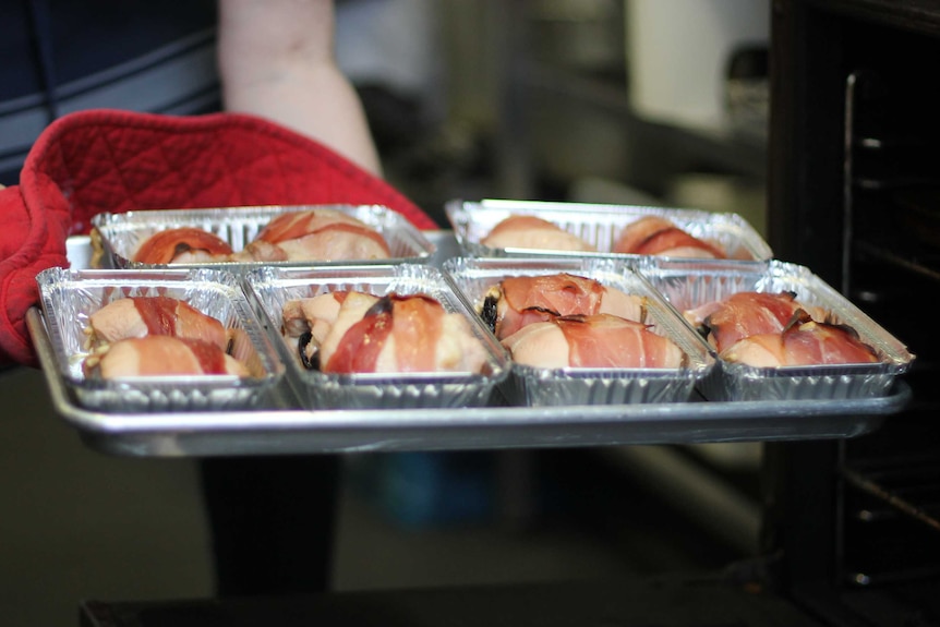 hands with oven glove carrying tray of chicken out of oven