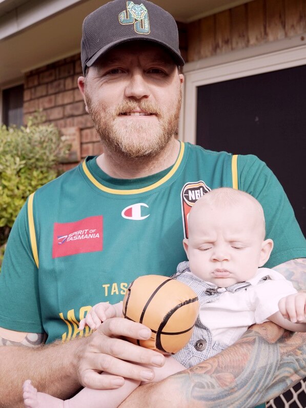 A man in a cap gives a baby in his arms a toy basketball