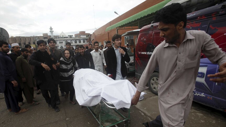 A man wheels a body of a woman who died in an earthquake in Peshawar, Pakistan
