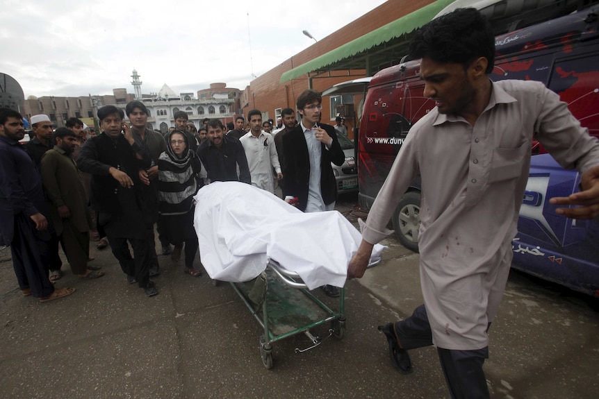 A man wheels a body of a woman who died in an earthquake in Peshawar, Pakistan