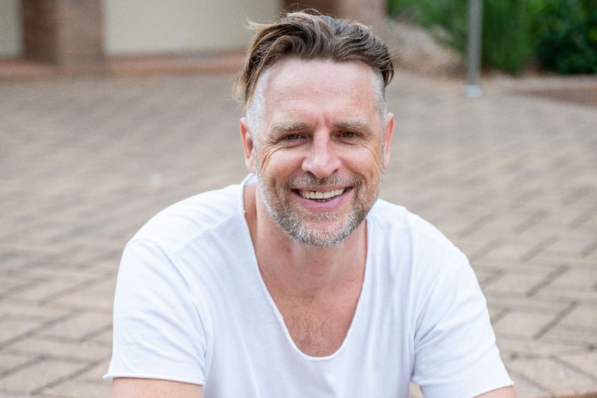 A man in a white shirt smiling while sitting on steps