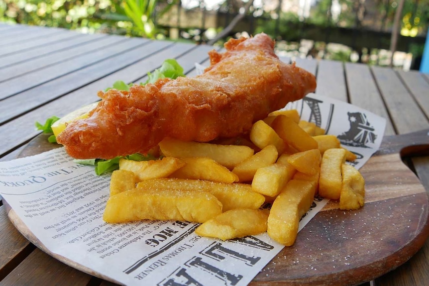 Battered Barramundi and chips on a wooden plate.