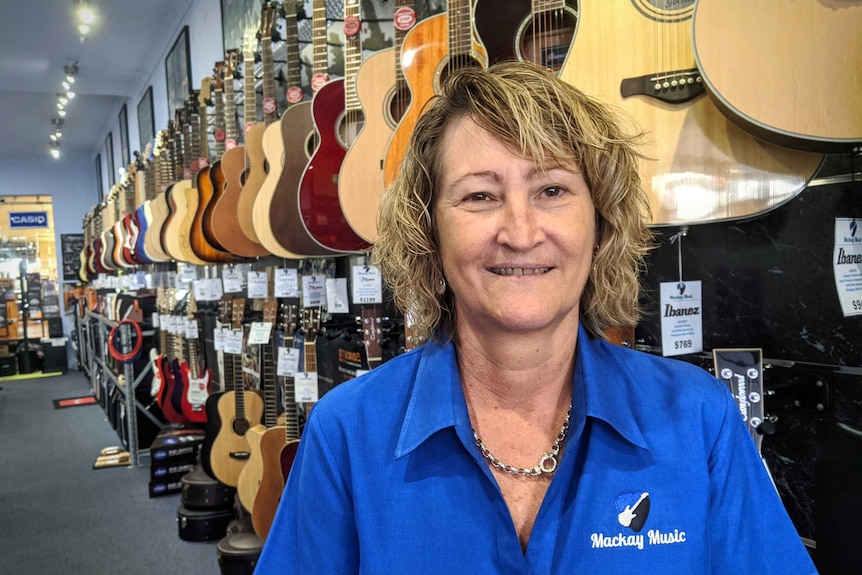 A woman stands in front of guitars on a wall