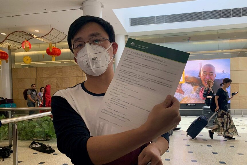 A man wearing a mask holds up an information sheet