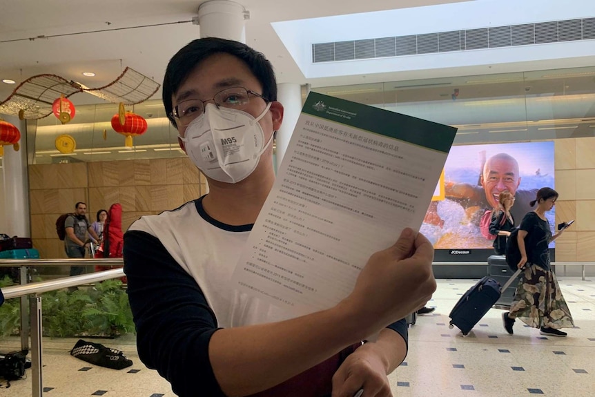 A man wearing a mask holds up an information sheet