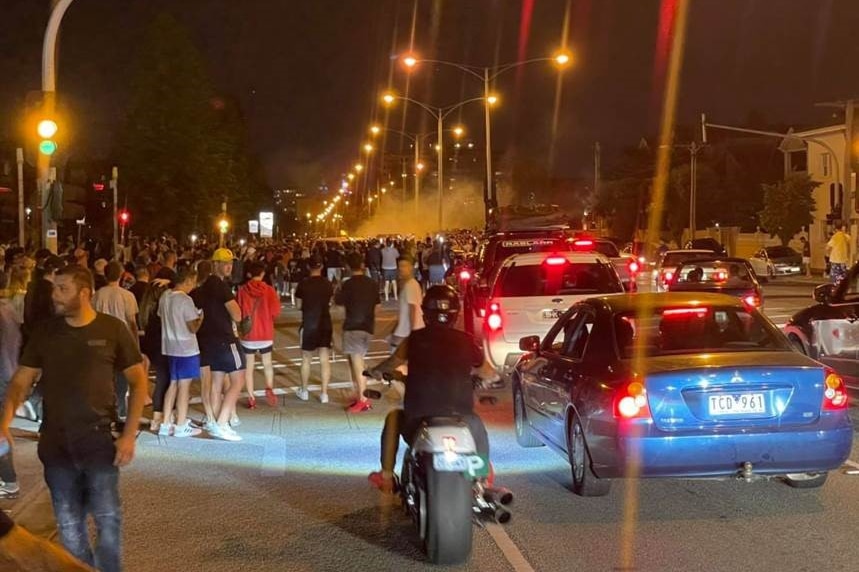 A large crowd around a street intersection at night.