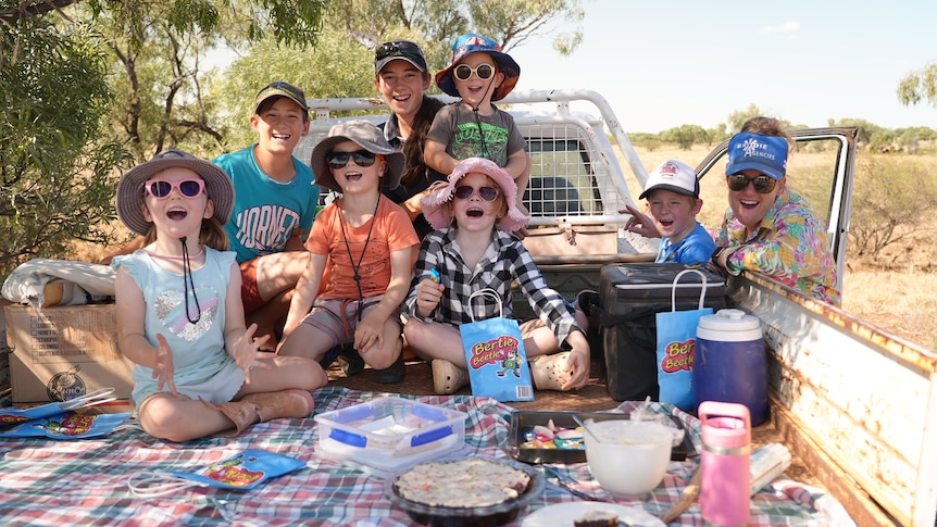 Seven young children sit in the tray of a ute surrounded my lollies and showbags with woman standing next to them, smiling