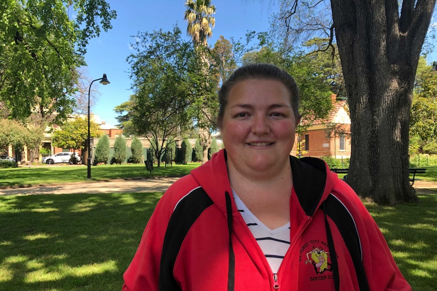 A woman stands with parkland behind her.