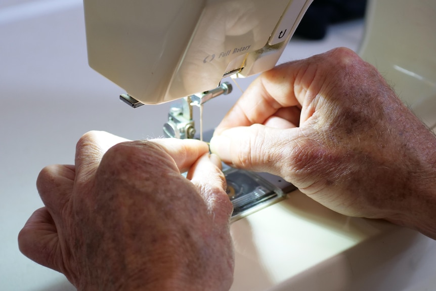A man's hands threading a sewing machine.