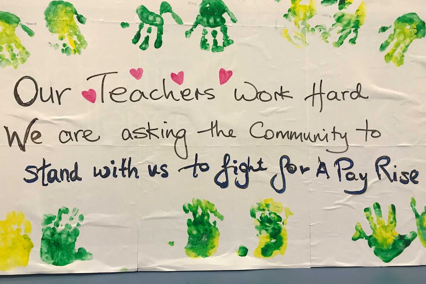 A sign bordered by children's handprints asks for support for childcare workers' fight for better pay.