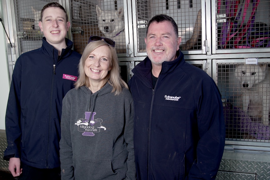 Three people with dogs in cages behind them.