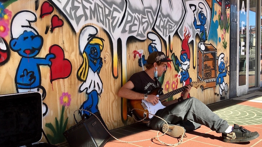 busket playing music in front of grafitti