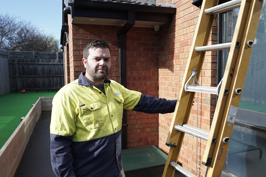 Kevin Schafer wearing a high-vis shirt and holding a steel ladder outside a brick home.