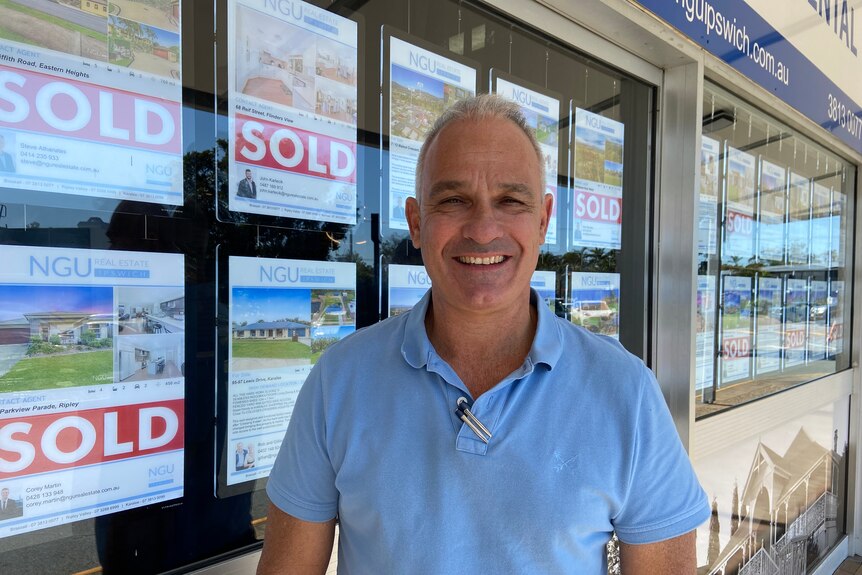 A smiling man in front of a real estate window.