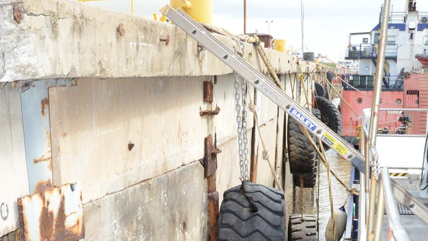 The gap between a barge and a wharf wall showing a rope, tyre and a ladder.