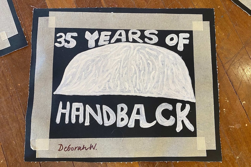 A painting of Uluru with the words '35 years of handback' around it. The painting is black and white.