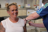 A tattooed woman smiles whilst having her COVID vaccine administered.