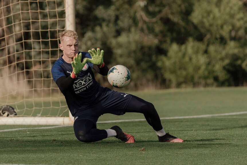 A goal keeper reaching out for a soccer ball in front of the goals