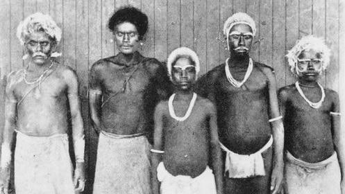 Black-and-white photo shows five Solomon Islander men standing in a line after being recruited to work on plantations.