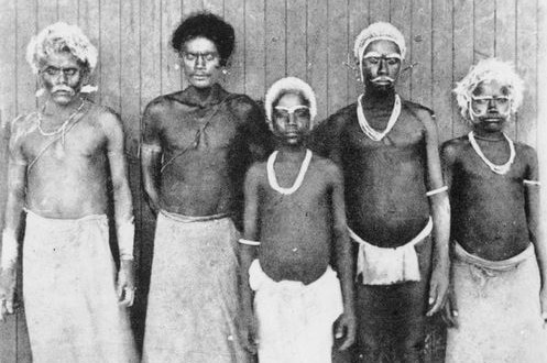 Black-and-white photo shows five Solomon Islander men standing in a line after being recruited to work on plantations.