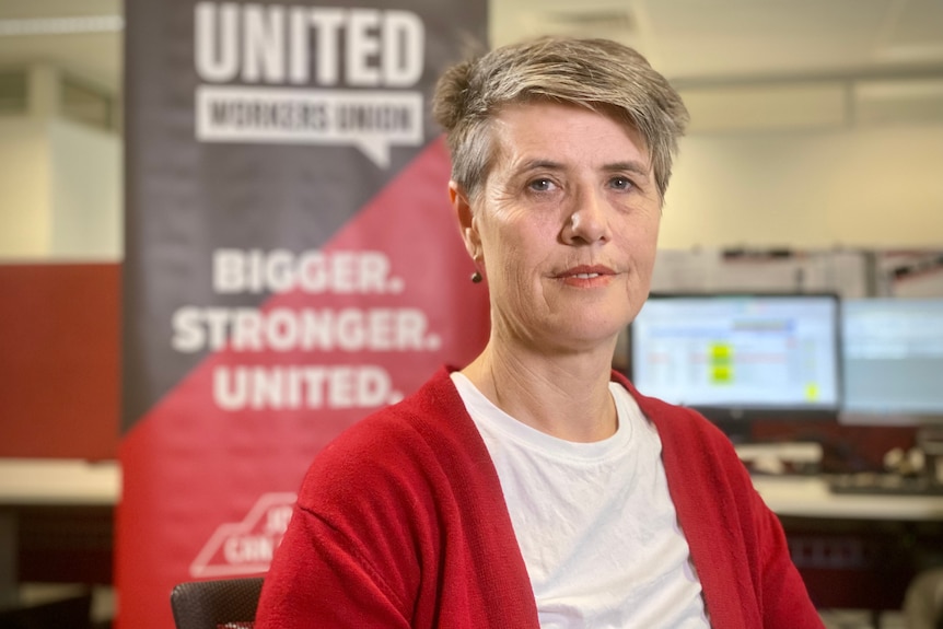 Carolyn Smith wearing a red cardigan in an office, in front of large black and red United Workers Union sign.