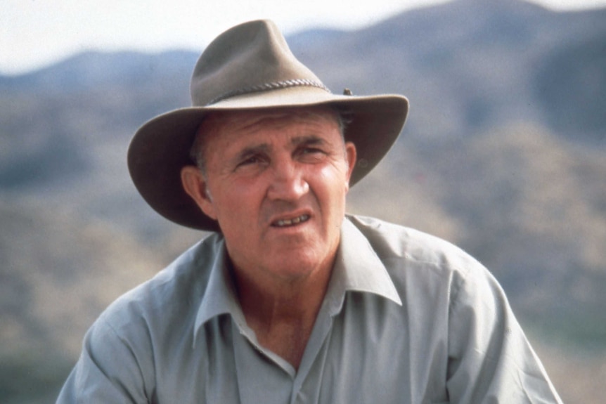 A man wearing an Akubra squints against a mountain backdrop.