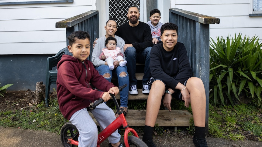 The family of six sit on the front steps of their first home