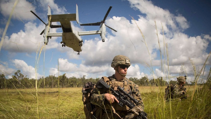 A soldier stands with a gun under a helicopter.