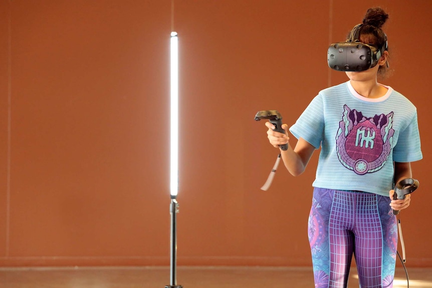Young woman using virtual reality technology including headgear and controllers.